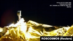 Снимка, направена от камерата на лунния апарат за кацане "Луна-25" по време на полета му до Луната, показва емблемата на мисията и кофата за събиране на проби на лунния комплекс