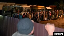 Мъж наднича през ограда към строени през нощта мобилизирани руски войници в Тара, Омска област, 26 септември 2022 г.