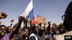 Жители на столицата Уагадугу развяват знамето на Русия. До него се вижда плакат, на който пише "Не на Франция".