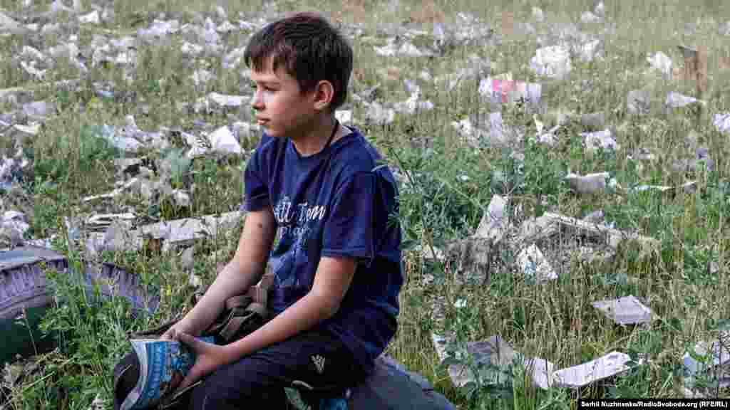 Васил седи в двора, заобиколен от останките на училището му след обстрела.