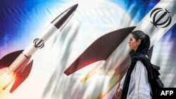 Жена преминава край плакат с ракети, носещи емблемата на Ислямска република Иран, Техеран, 15 април 2024 г.