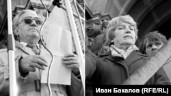 Блага Димитрова, писател, дисидент и по-късно вицепрезидент, заедно с Анжел Вагенщайн, кинорежисьор и член на БКП, на стъпалата на храм-паметника "Св. Александър Невски" пред петдесетхилядно множество на първия свободен митинг, 18 ноември1989 г. По-късно политическите убеждения ще разделят писателката и режисьора. Разделителната линия задълго ще остане в българското общество. Много знакови фигури на прехода ще преминават на "другата страна".