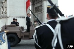 Президентът на Франция Еманюел Макрон и началникът на Генералния щаб на отбраната на Франция генерал Тиери Буркхард (в средата) във военен автомобил, докато правят преглед на войските по време на церемонията за 80-годишнината от Деня на победата в Европа.