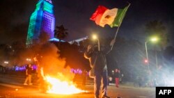  Протестиращ развява мексиканското знаме на фона на сблъсъци с органите на реда по улиците около федералната сграда по време на протестa след амтиимиграционни акции в Лос Анджелис, Калифорния. 